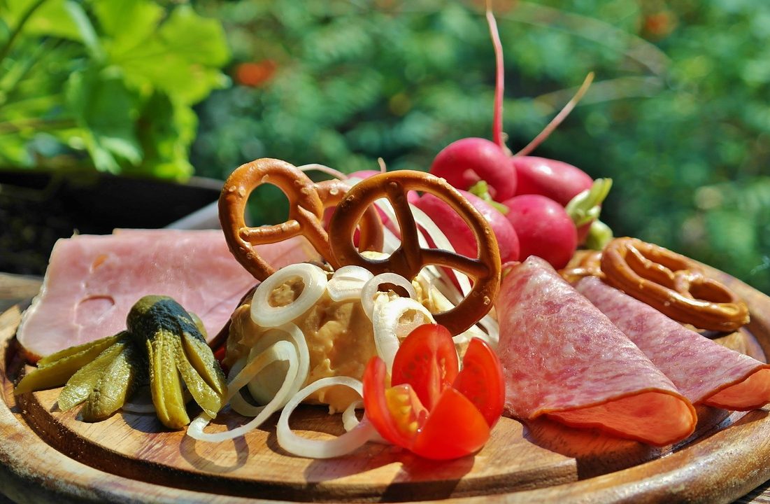 Brotzeiten Bunte Vesperplatte mit Wurst, Käse, Brezeln, Radieschen, Zwiebeln und Krustenbrot.